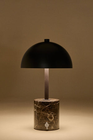 Nicolas wireless LED lamp – lifestyle shot placed on a book on a white surface beside a marble tray, lamp lit, small scale visible