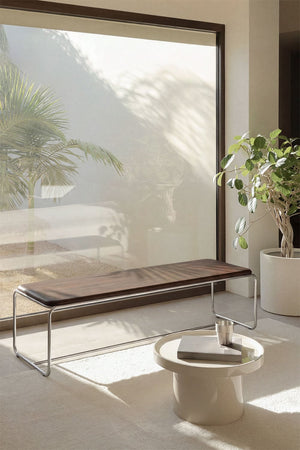Altrex bench – lifestyle shot by large window with plant, dark acacia wood and stainless steel frame