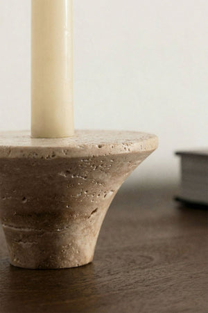 Bellvion travertine candle holder – lifestyle shot on dark walnut sideboard with lit cream taper candle, hardcover book in background, warm ambient light