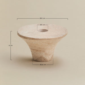 Bellvion travertine candle holder – lifestyle macro on dark walnut surface, cream taper candle inserted, dark book visible at right, warm pooled light on stone surface