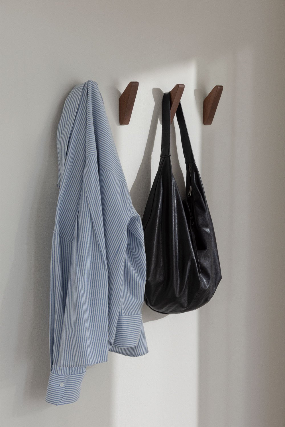 Brana wooden wall hooks – lifestyle shot of three dark walnut hooks mounted on a light wall, blue striped shirt and black leather bag hanging from two of them