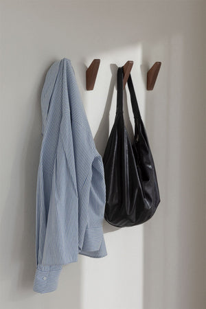 Brana wooden wall hooks – lifestyle shot of three dark walnut hooks mounted on a light wall, blue striped shirt and black leather bag hanging from two of them