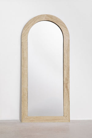 Alune arched mirror – lifestyle shot leaning against warm plaster wall with armchair beside it