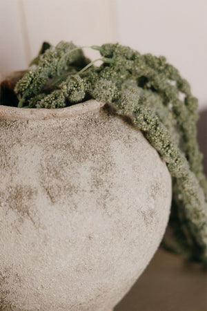 Filis ceramic vase – lifestyle shot on a Kinfolk book on a dark shelf beside abstract wall art panels, styled with dried green amaranth cascading from the opening